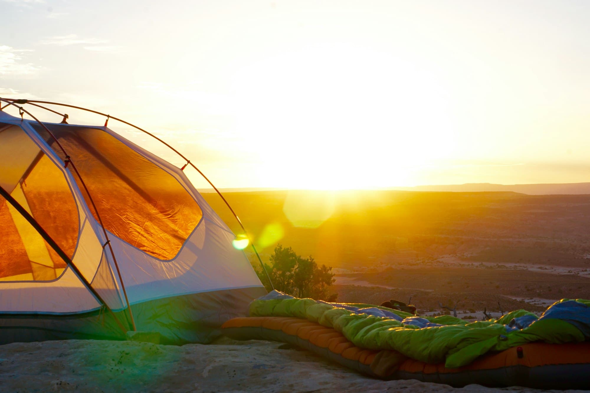 A tent catching first light at sunrise on a clifftop